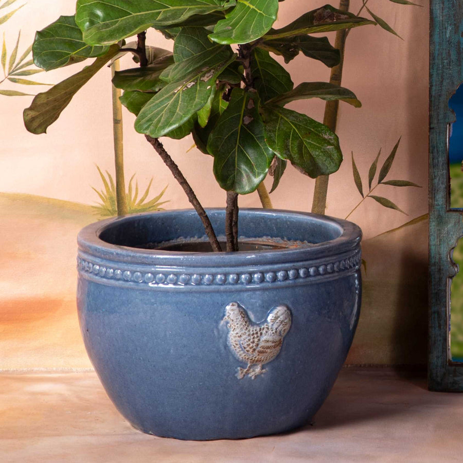 Decorative shelf with decorative items, plant, and stool against a wall with bird design.