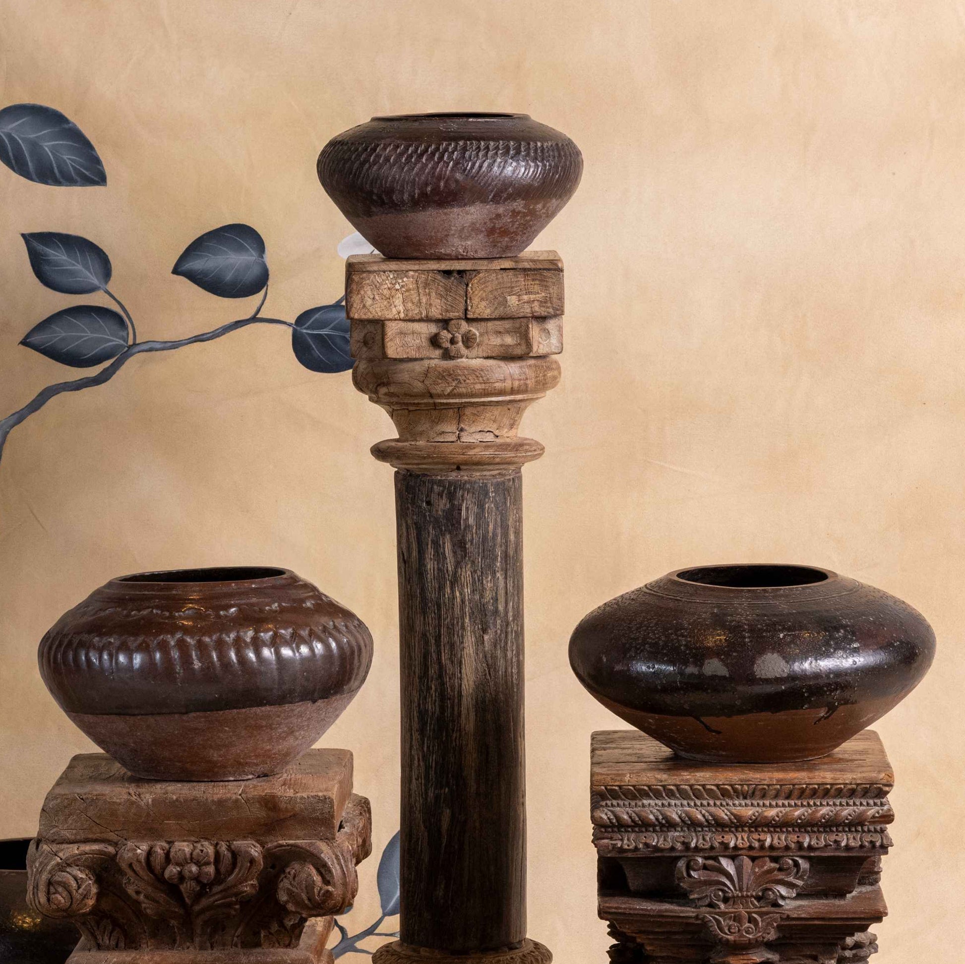 Set of wooden vases and candle holders against a decorative wall with floral patterns.