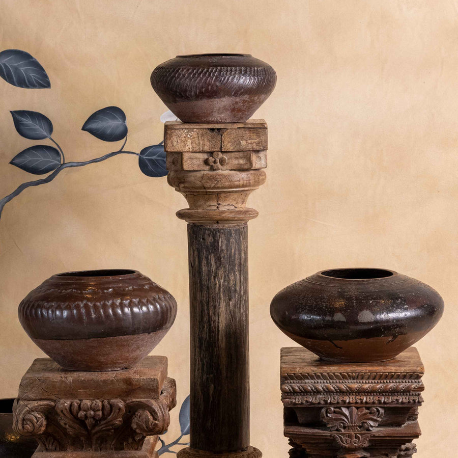 Set of wooden vases and candle holders against a decorative wall with floral patterns.